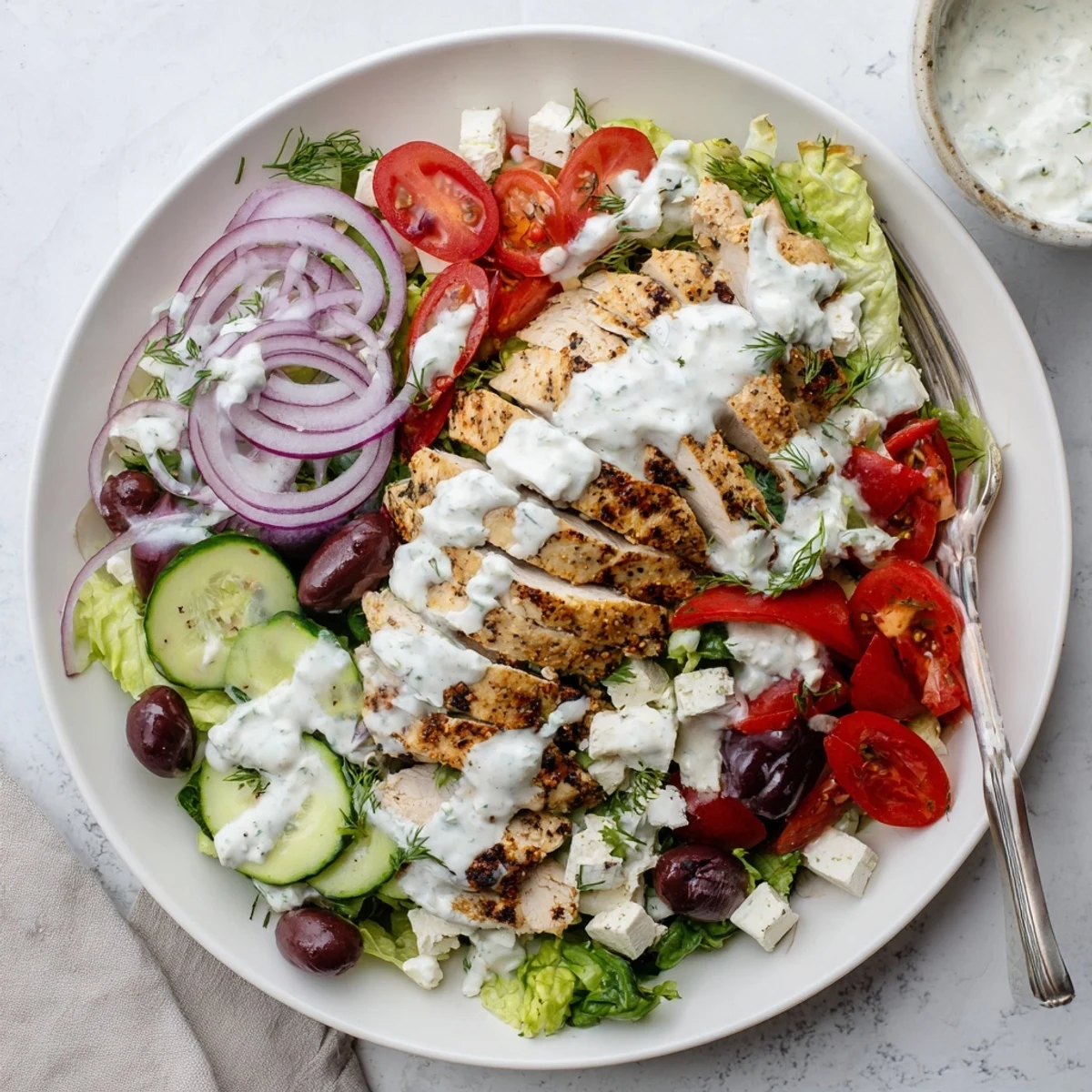 Greek-style tzatziki chicken salad plated with cherry tomatoes, Kalamata olives, cucumber, and crumbled feta cheese drizzled with dressing