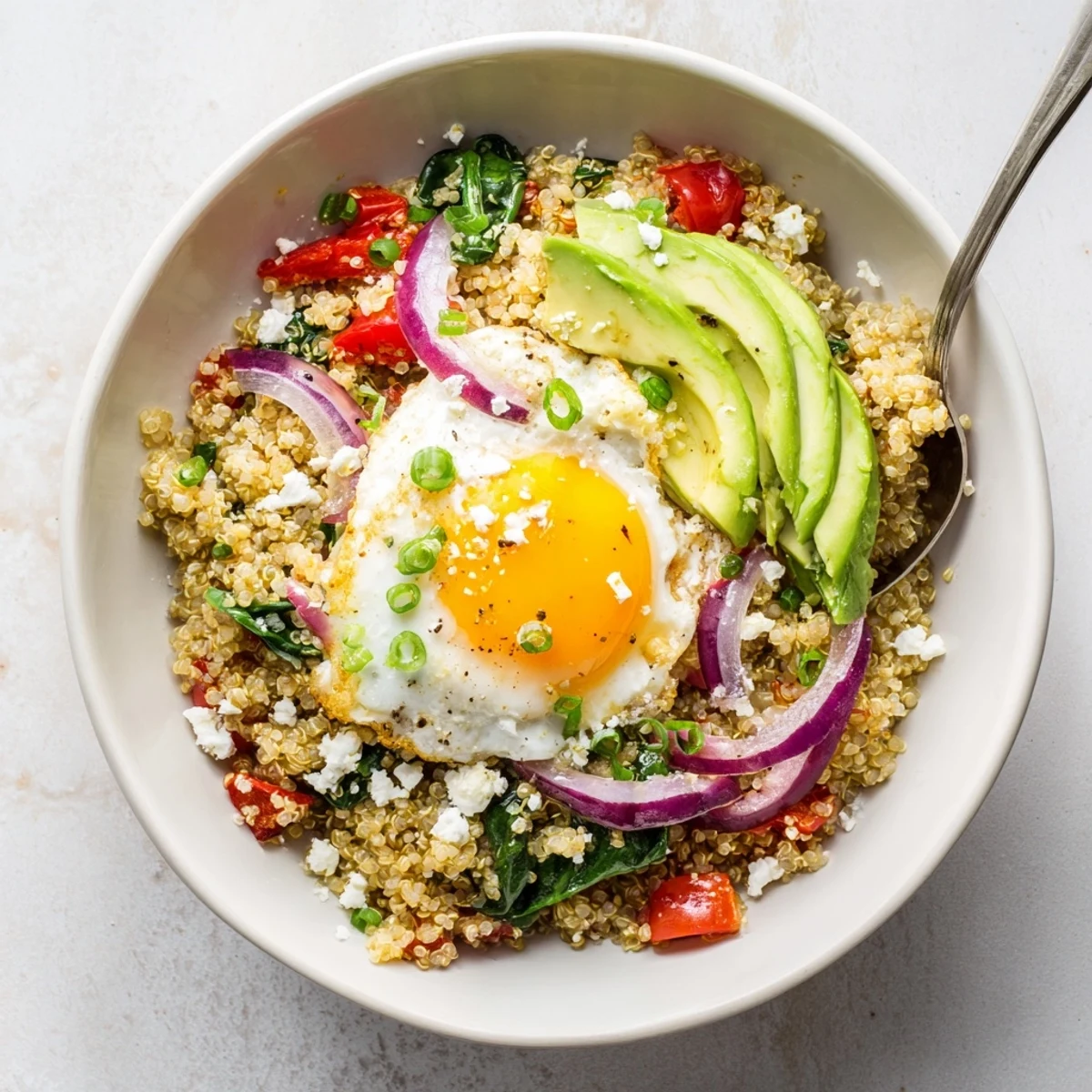 Protein-rich savory quinoa breakfast bowl featuring wilted spinach, cherry tomatoes, and runny yolk