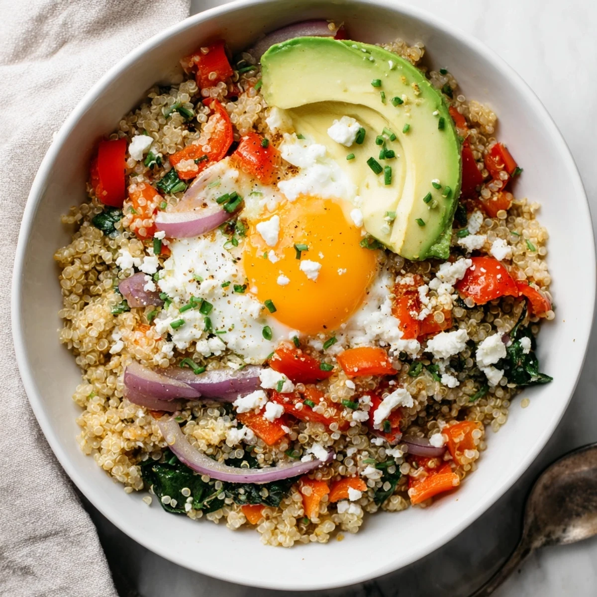 Golden fried egg resting atop fluffy quinoa breakfast bowl with colorful sautéed vegetables