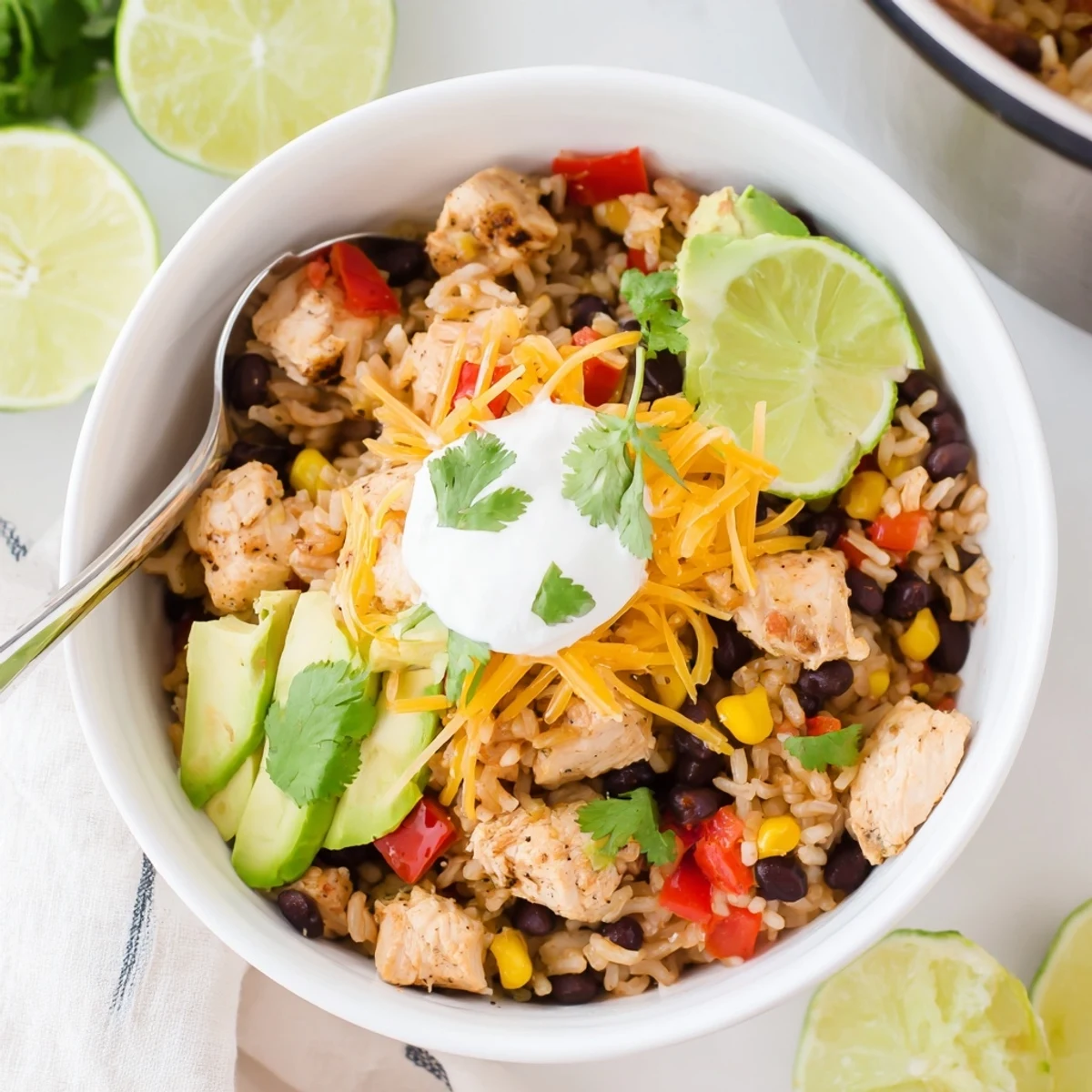 Heaping bowl of Instant Pot chicken burrito bowls garnished with sour cream, lime wedges, and cheese