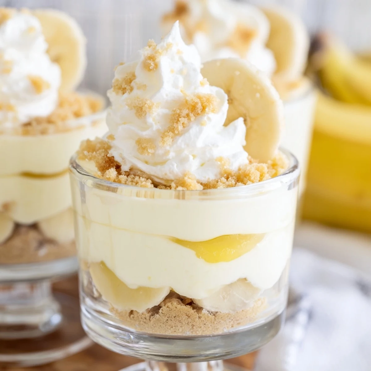 Individual no bake banana pudding cheesecake cups topped with golden wafer crumbs and sliced bananas