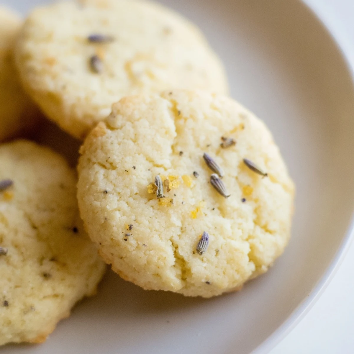 Golden lemon lavender cookies with speckled lavender buds on a rustic white plate
