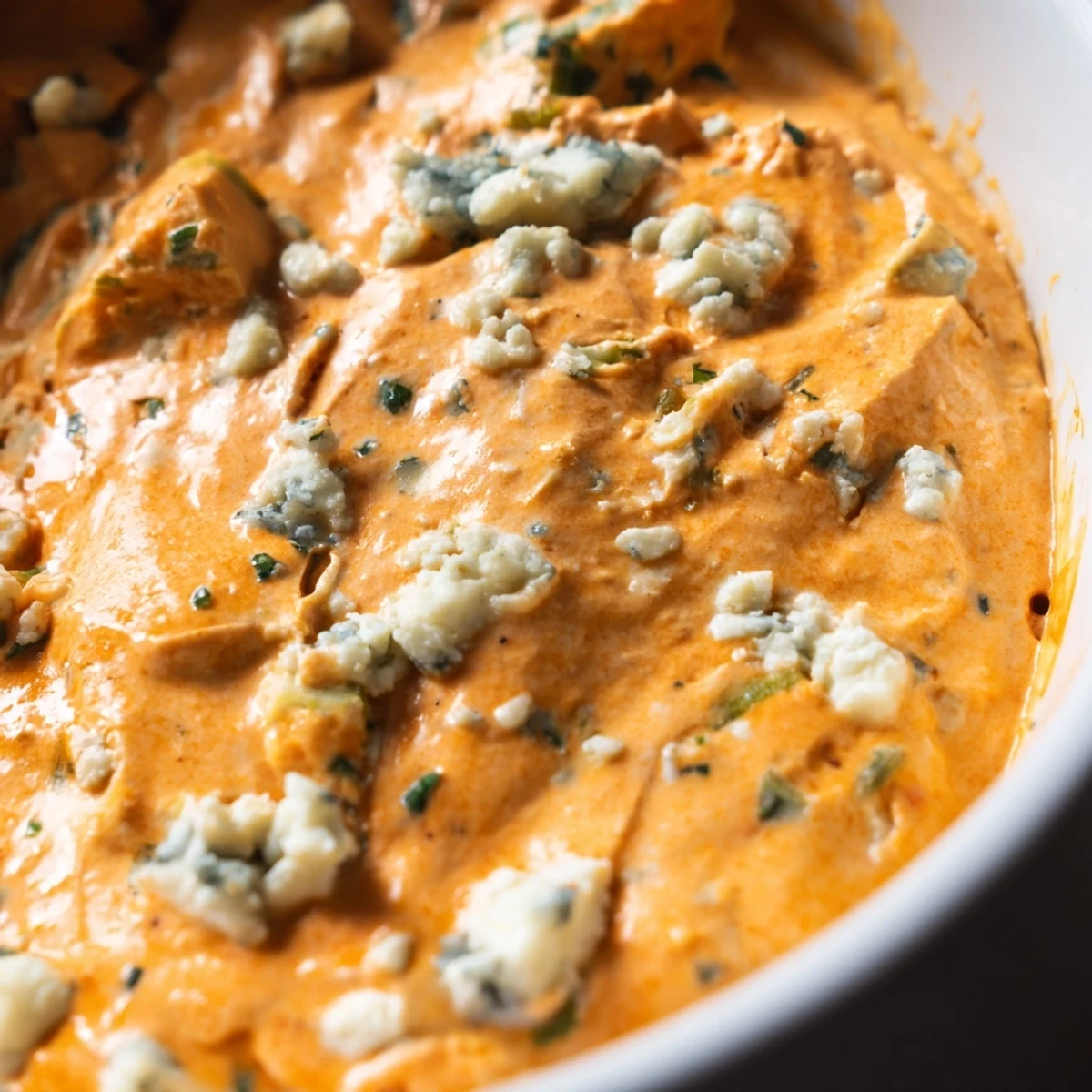 Creamy buffalo pickle dip in a serving bowl surrounded by crispy chips and fresh veggie sticks