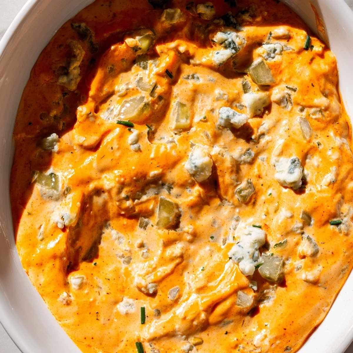 Tangy buffalo pickle dip topped with cheddar cheese and fresh chives in a rustic bowl