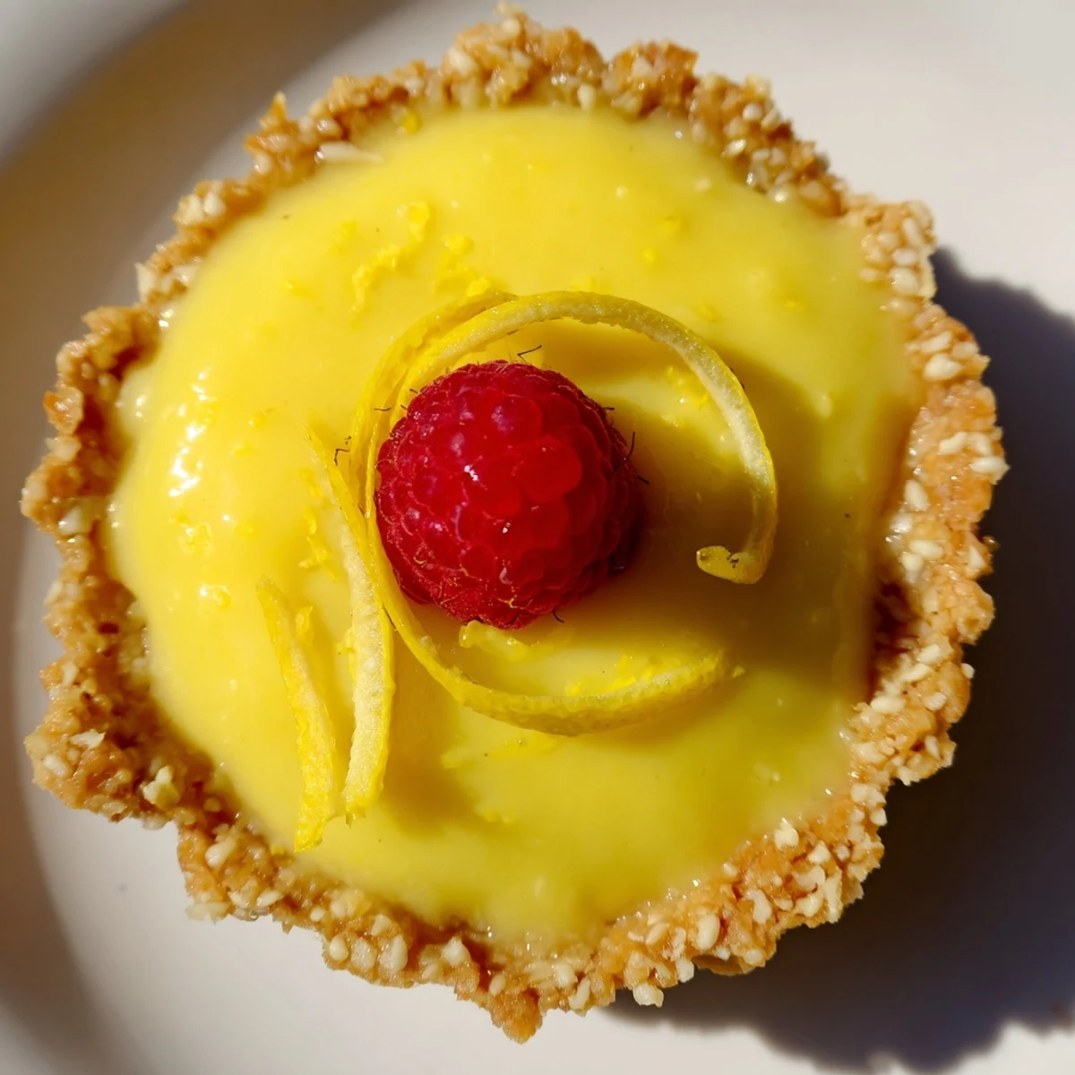 Golden mini vegan lemon tarts topped with fresh berries on a white serving plate
