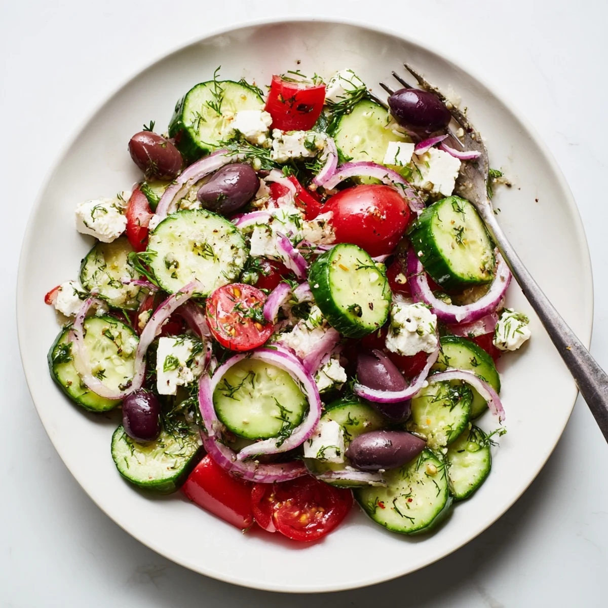 Vibrant Mediterranean cucumber salad plated with juicy tomatoes, olives, and crumbled feta cheese topping