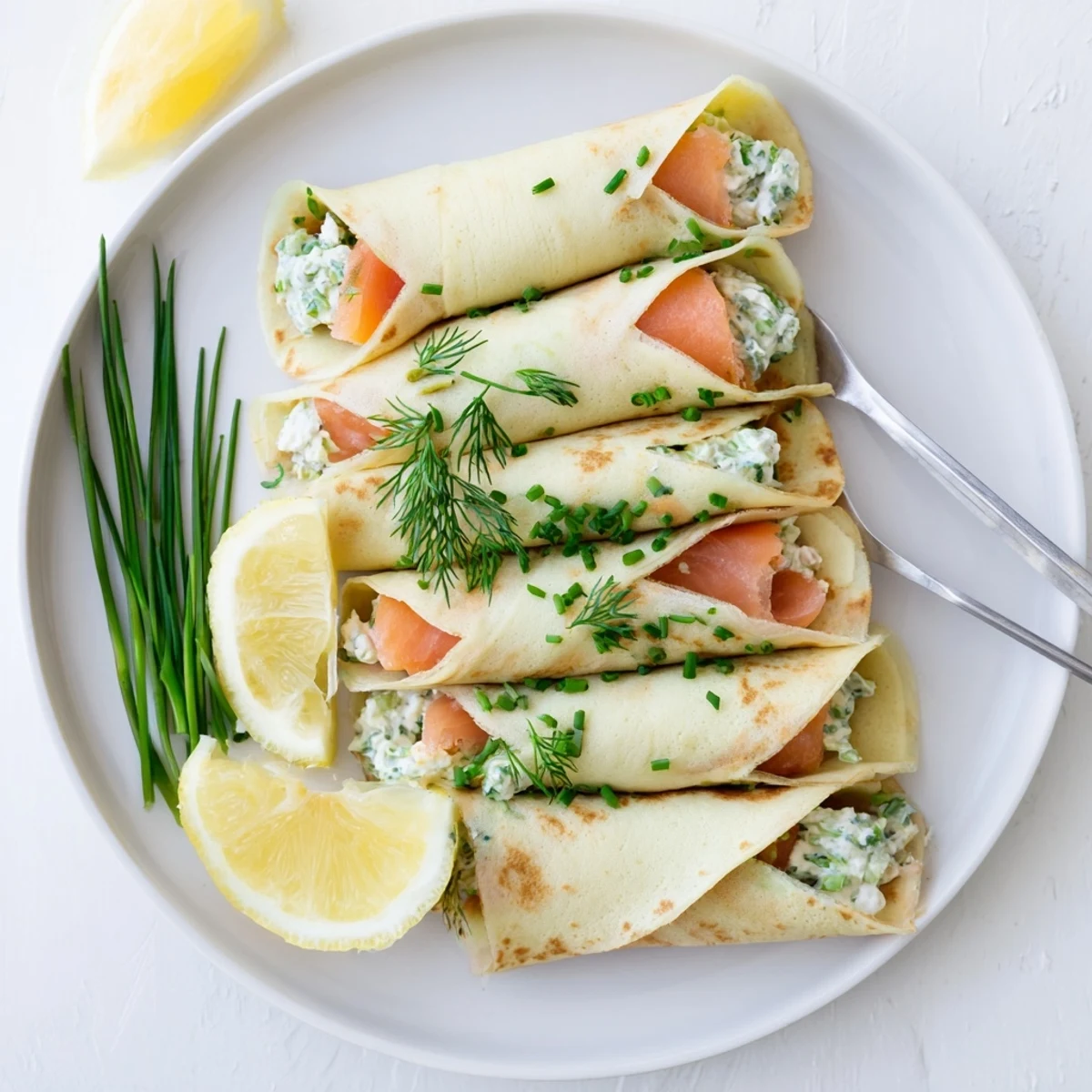 Elegant smoked salmon crepes plated with lemon wedges and sprinkled chopped chives
