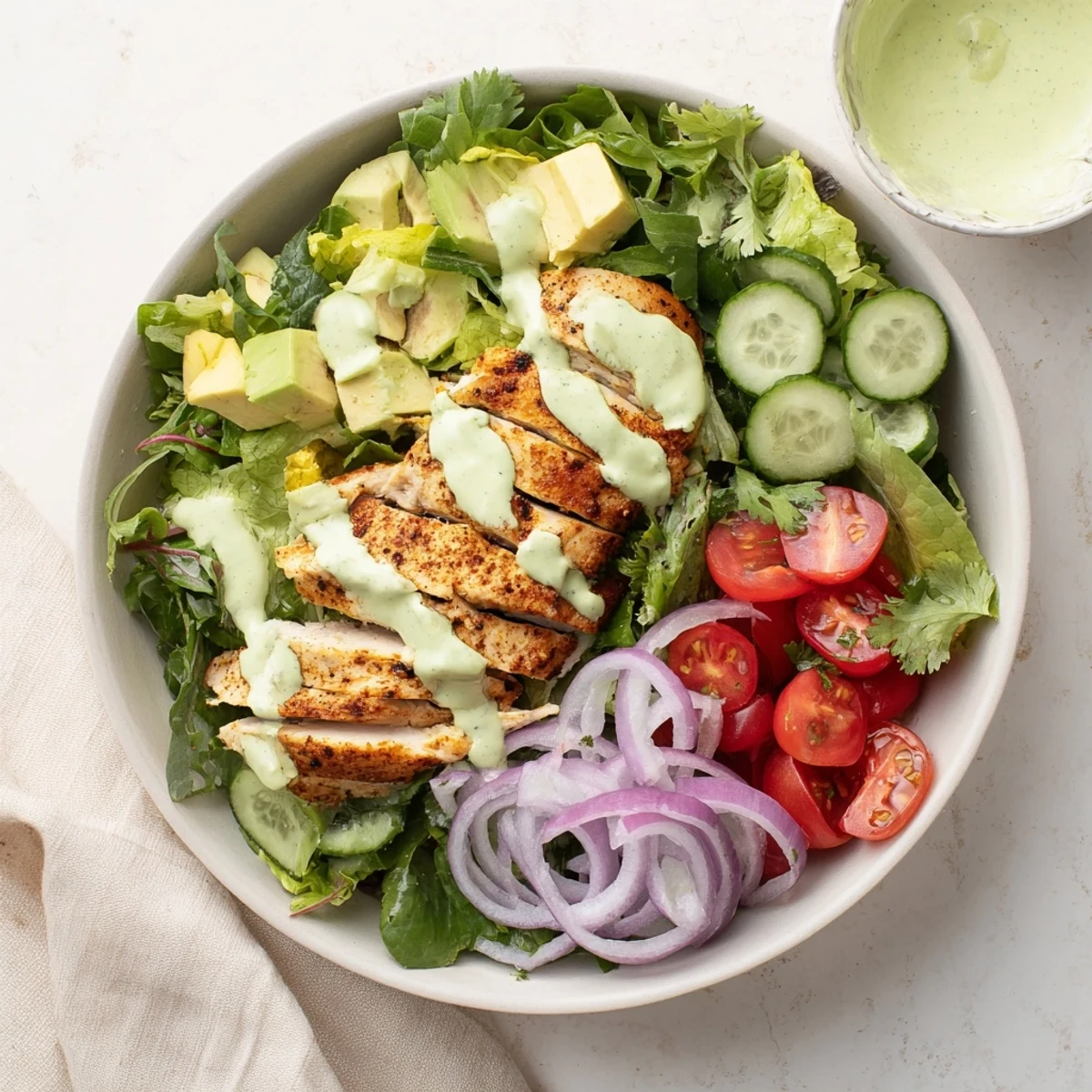 Vibrant creamy avocado grilled chicken salad bowl with juicy sliced chicken, fresh vegetables, and rich avocado dressing.