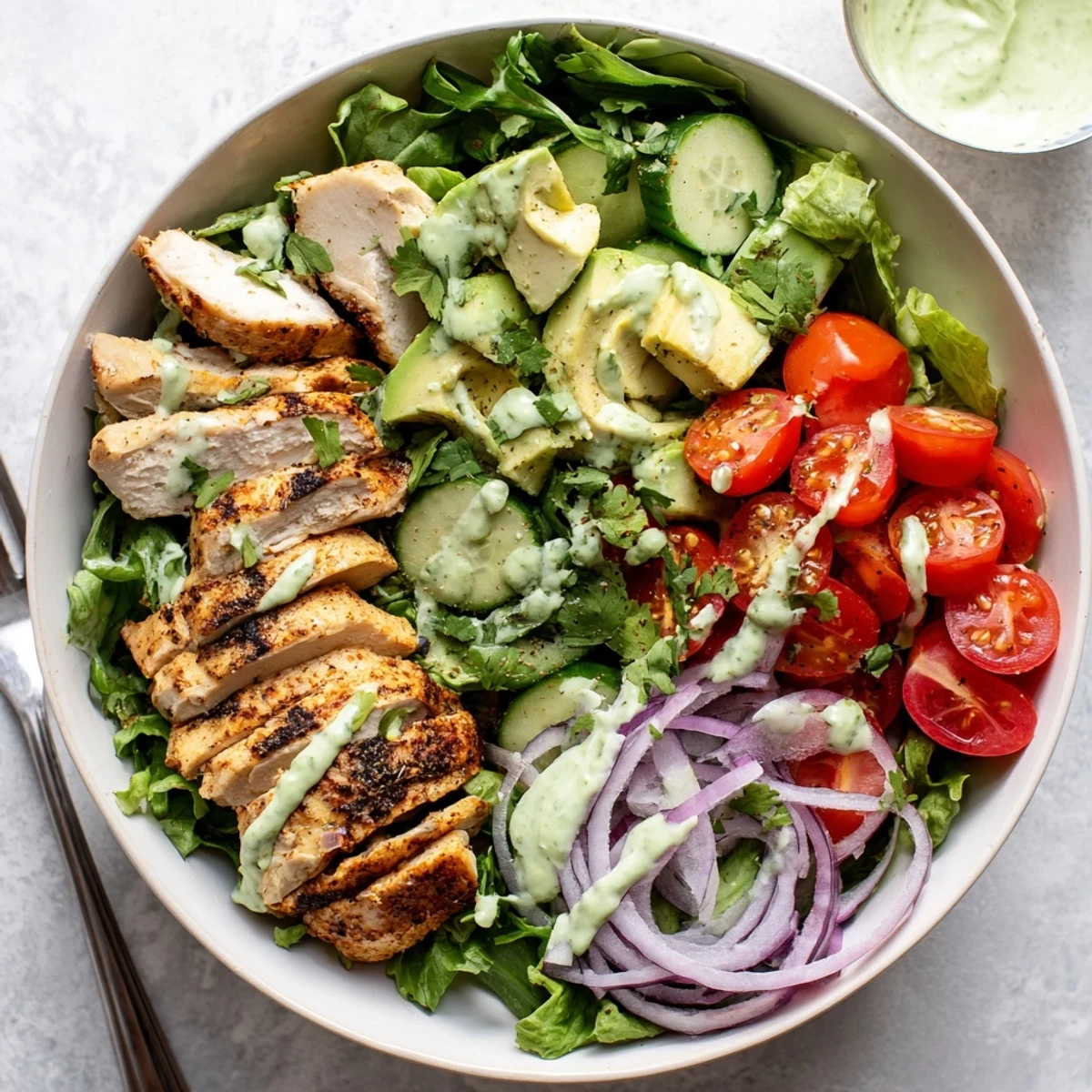 Colorful bowl featuring grilled chicken strips, creamy avocado chunks, crisp greens, and tangy avocado lime dressing.