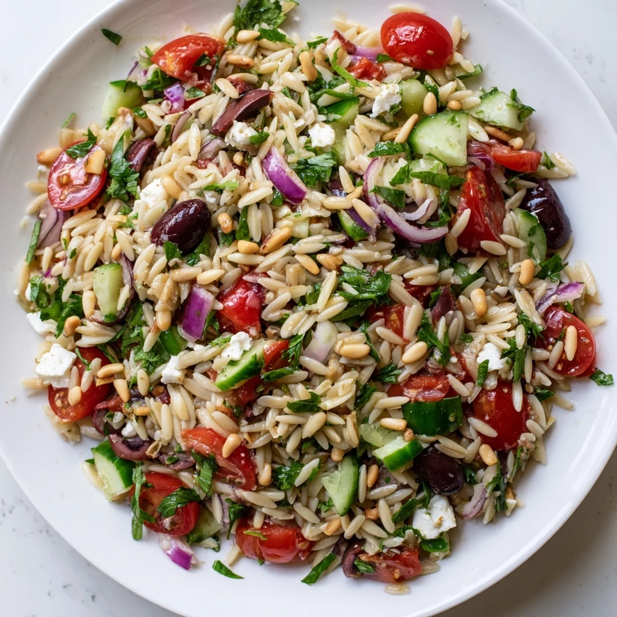 Colorful Mediterranean orzo power salad bowl topped with crumbled feta and fresh vegetables