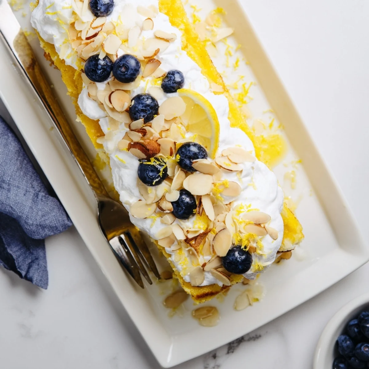 Slice of refreshing lemon blueberry poke cake showing creamy layers and scattered almonds against a bright yellow background