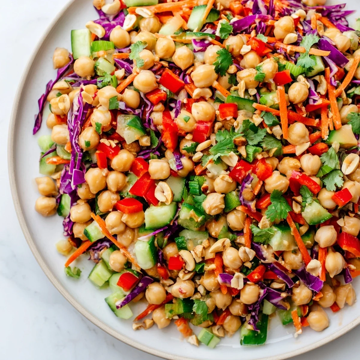 Crunchy Thai chickpea salad in a white bowl drizzled with creamy peanut dressing